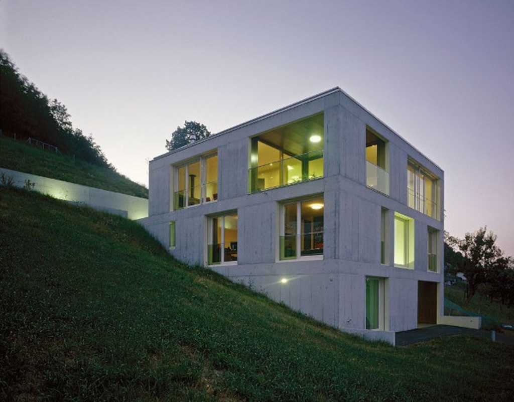 Дизайн двухэтажного коттеджа простой геометрической формы удивительно гармонично смотрится на фоне склона